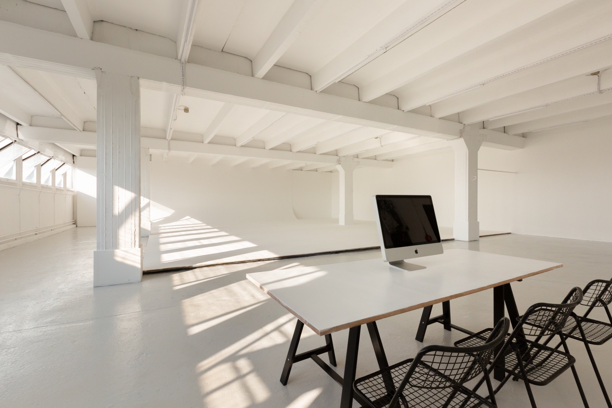 Picturepool Studios interior — desk on sawhorses with an Apple iMac and black wire chairs, white walls and exposed ceiling beams