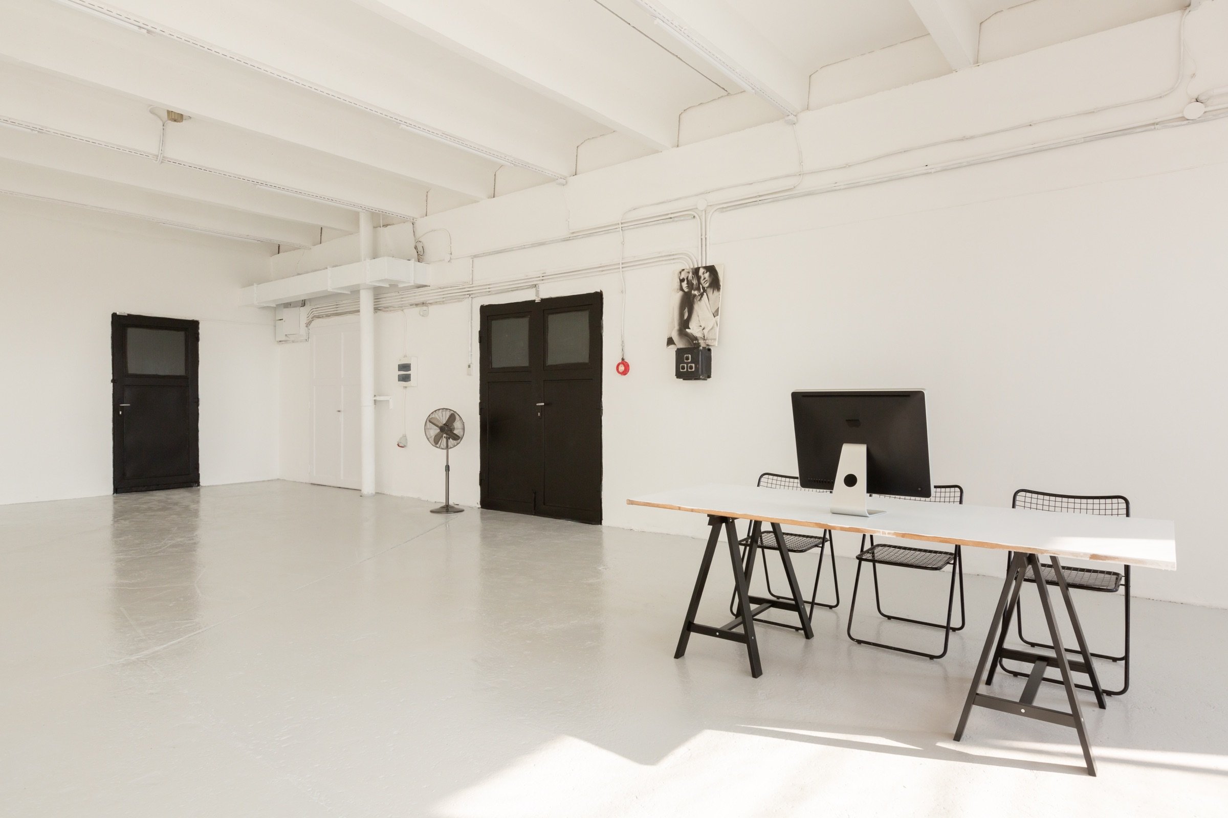 Picturepool Studios interior — desk on sawhorses with a monitor and chairs, black double doors and a standing fan